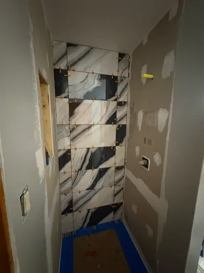 Alcove shower mid-tile-installation with bold marble-look porcelain and leveling clips still in the joints