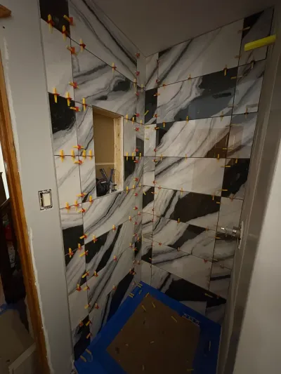 Shower walls mid-installation with black and white marble-look porcelain tile and leveling clips still attached.