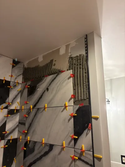 Marble-look porcelain shower wall mid-installation with red and yellow tile leveling clips still in place.