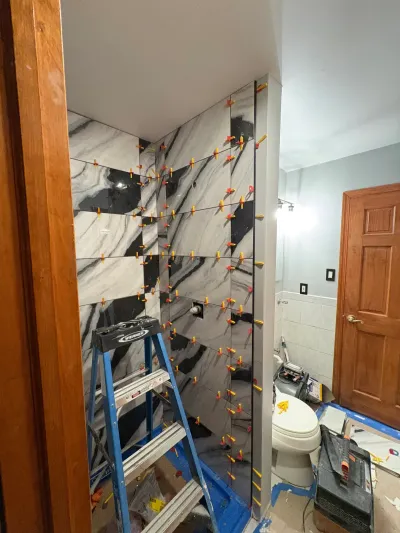 Bathroom shower walls mid-tiling with black-and-white marble-look porcelain and leveling clips still in place.