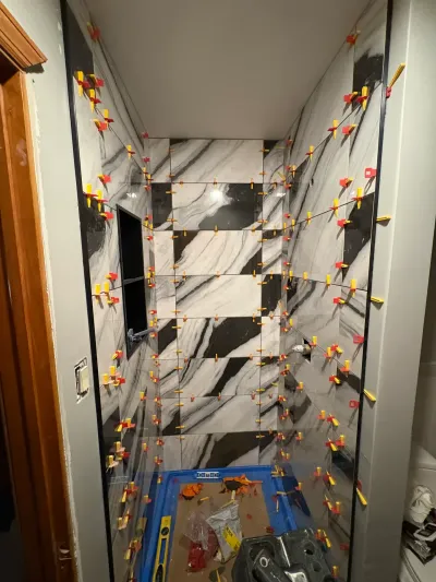 Walk-in shower mid-tiling with black-and-white marble-look porcelain panels and leveling clips in every joint