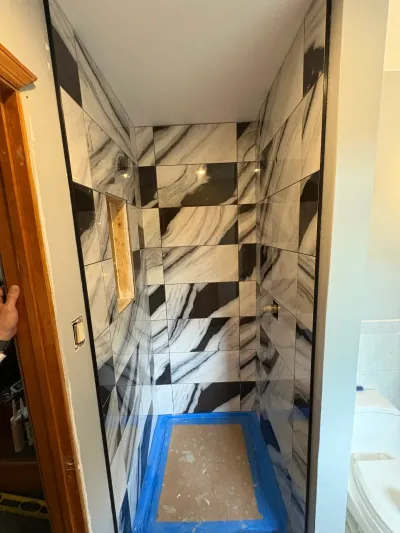 Alcove shower mid-tiling with black and white marble-look checkerboard tile and a taped-off floor.