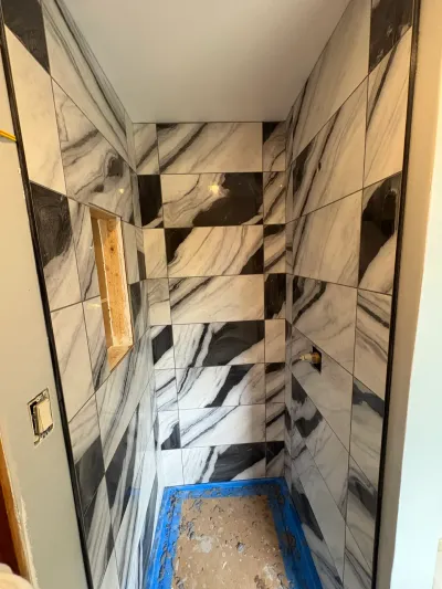Walk-in shower mid-tiling with black and white marble-look porcelain walls and an untiled mortar pan