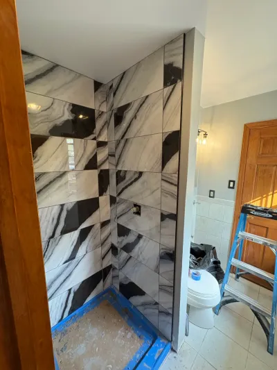 Corner walk-in shower tiled in bold black-and-white marble-look porcelain, with floor still taped off mid-remodel.