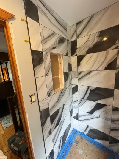 Shower walls tiled in black-and-white marble-look porcelain with an untiled recessed niche mid-installation.