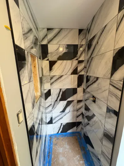 Walk-in shower mid-tiling with glossy black and white marble-look tile and an unfinished shower pan.