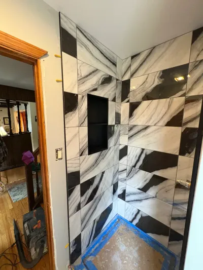 Walk-in shower under construction with black and white marble-look tile, built-in niche, and taped mortar floor.