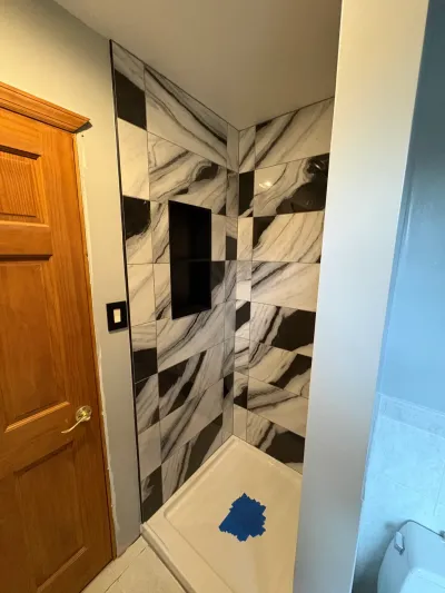 Corner shower under construction with black and marble-look checkerboard tile, black niche, and white base.