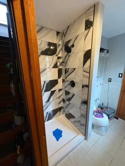 Walk-in shower tiled in black-and-white marble-look porcelain with matte black fixtures, mid-remodel.