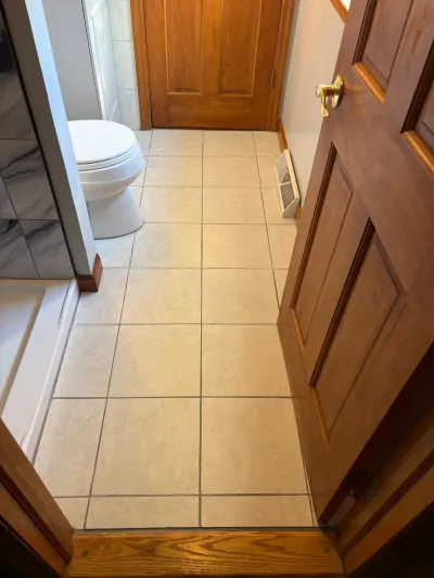 Small bathroom with diagonal beige tile floor, white toilet, glass shower and honey oak door trim.