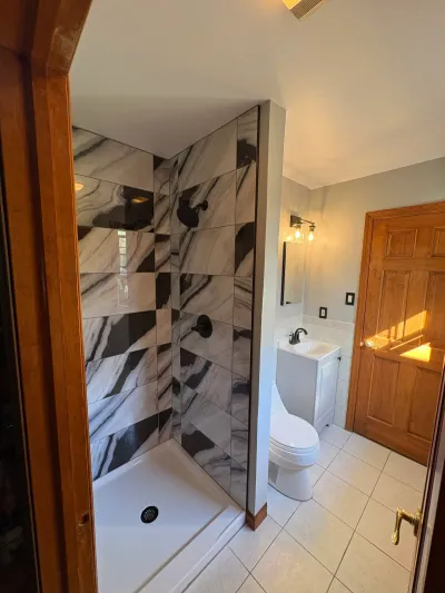 Small remodeled bathroom with black-and-white marble-look tile walk-in shower, matte black fixtures, and white vanity.