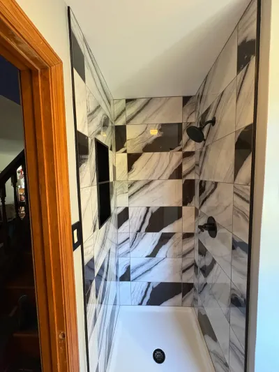 Walk-in shower tiled in black and white marble-look squares with matte black fixtures and a recessed niche.