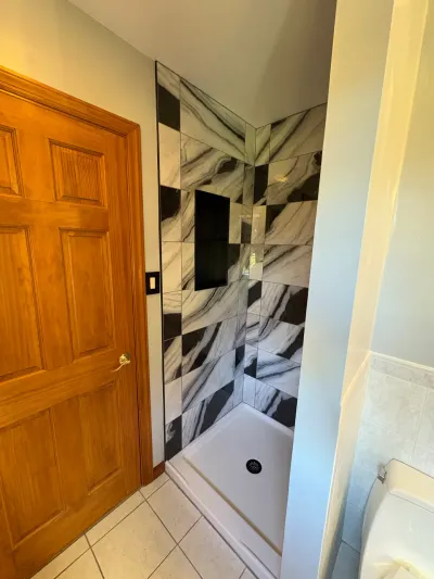 Walk-in shower tiled in black and white marble-look checkerboard with recessed niche beside an oak door.