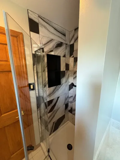 Walk-in corner shower with black and white marble-look tile, black niche, and frameless glass door.