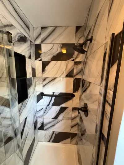 Walk-in shower tiled in bold black-veined marble-look porcelain with oil-rubbed bronze fixtures and glass door.