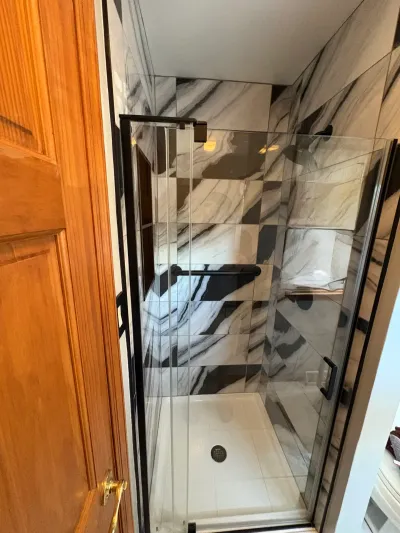 Frameless glass walk-in shower tiled in bold black-and-white marble-look porcelain with matte black hardware.