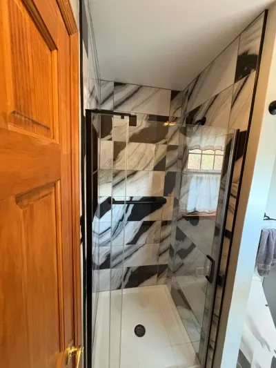 Walk-in shower tiled in bold black-and-white marble-look porcelain with a matte black framed glass door.