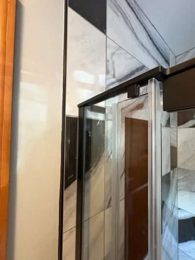 Close-up of a bronze-framed sliding glass shower door against marble-look large-format porcelain tile.