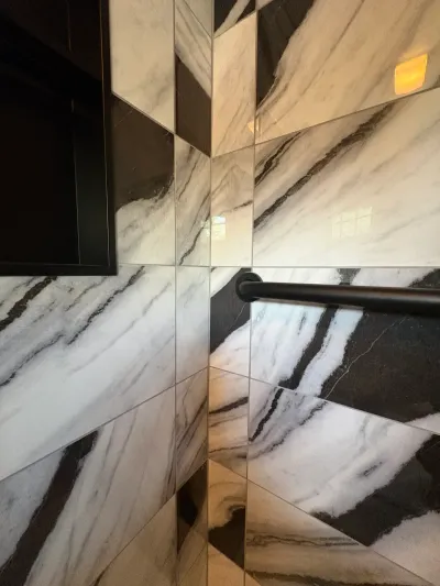 Close-up of a shower corner tiled in glossy black-and-white marble-look porcelain with a matte black grab bar.