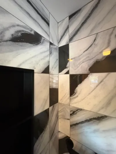 Corner detail of glossy white and gray marble-look porcelain wall tile running to the ceiling in a bathroom.