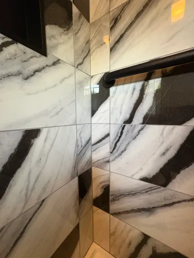 Polished black-and-white veined large-format shower tile in a corner with a matte black grab bar.