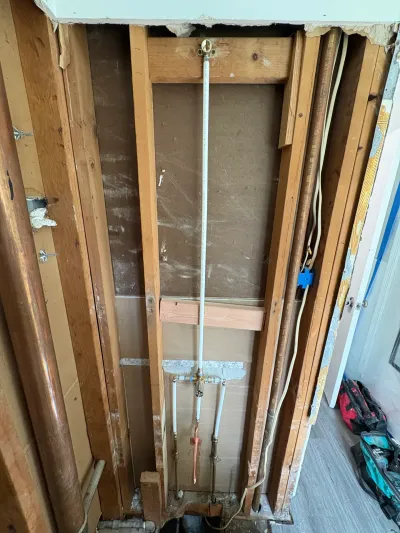 Bathroom wall stripped to studs with shower valve, PEX lines and copper pipe roughed in during remodel.
