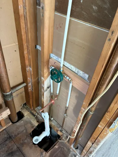 Gutted bathroom wall during plumbing rough-in with PEX lines, a green shutoff valve and copper piping.