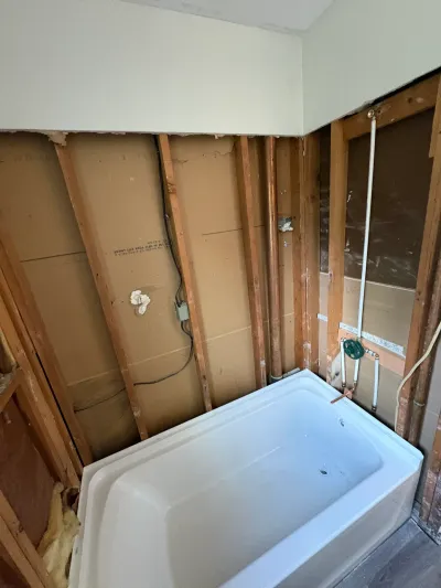 Bathroom stripped to wall studs with plumbing rough-in and a new white alcove tub set in place.