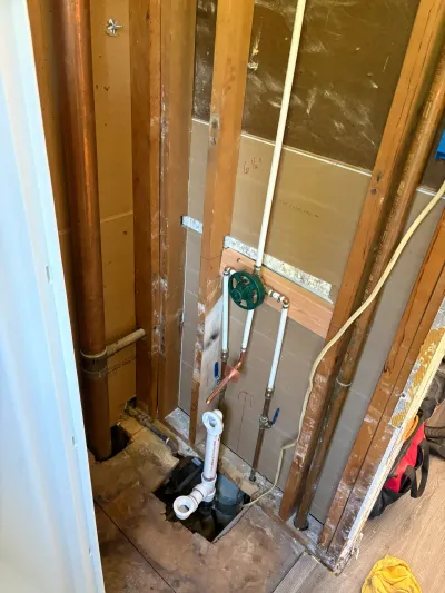 Bathroom plumbing rough-in with copper supply lines, shutoff valves, and PVC trap in an open floor cutout.