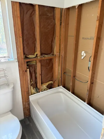 Bathroom mid-remodel with new white alcove tub set against walls stripped to studs and insulation.