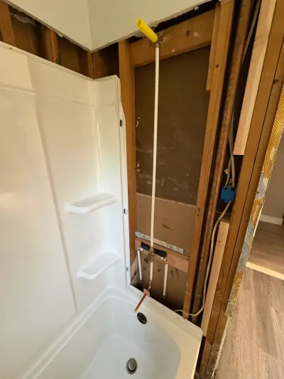 White fiberglass tub surround installed beside an open stud wall with exposed PEX plumbing and wiring.