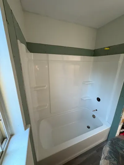 White fiberglass tub and shower surround newly installed in an alcove with green board still exposed above.