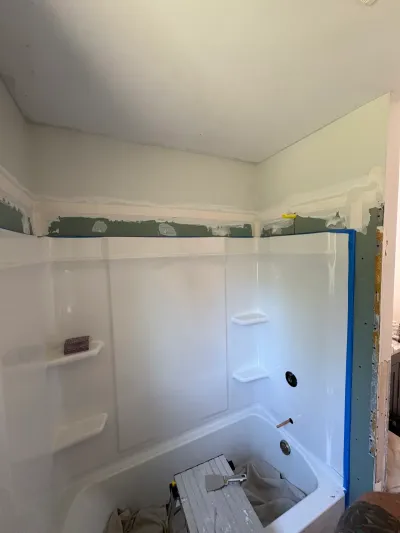 Bathroom under renovation with a new white tub surround and freshly taped drywall above it.