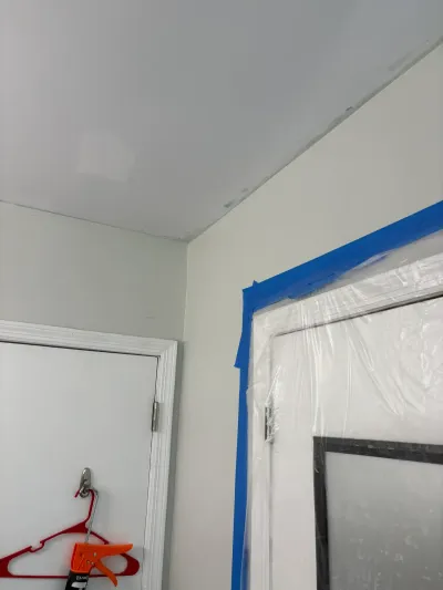 Room corner during painting prep, with one doorway masked in blue tape and clear plastic sheeting.