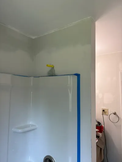 Bathroom mid-repaint with green paint above a taped-off white shower surround and a roller resting on top.