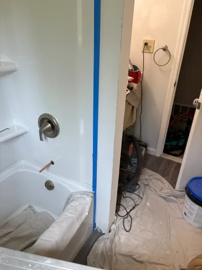 Bathroom mid-remodel with new white fiberglass tub surround, taped corner, drop cloths and shop vacuum.
