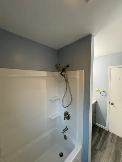 Remodeled bathroom with white alcove tub-shower, blue-gray walls, brushed nickel fixtures and wood-look plank floor.