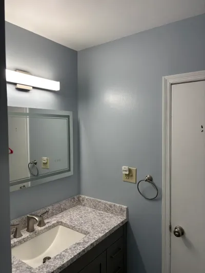 Small bathroom with blue-gray walls, dark shaker vanity, gray granite counter, framed mirror and LED light bar.