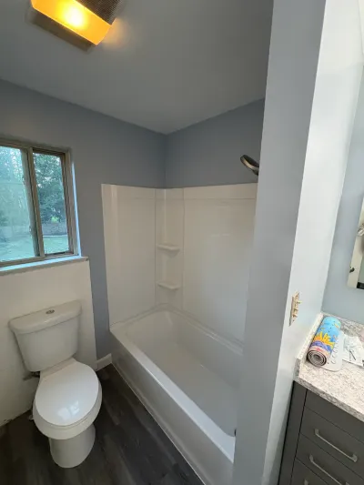 Remodeled bathroom with white alcove tub-shower, blue-gray walls, dark vinyl plank floor and gray vanity.