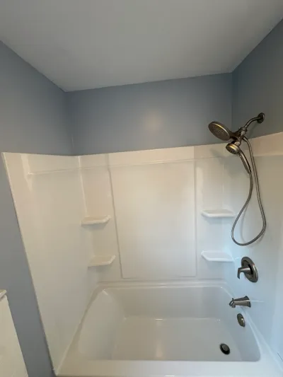 White acrylic tub surround and alcove bathtub with brushed nickel fixtures against gray-blue walls.