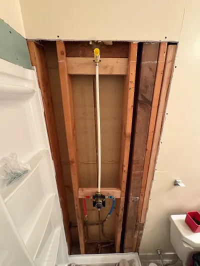 Bathroom wet wall opened to studs showing a new shower valve rough-in with red and blue PEX lines.