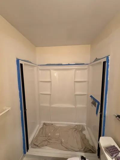 White fiberglass alcove shower surround masked with blue tape, drop cloth in the pan, door jambs installed.