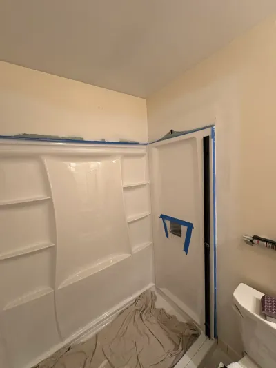 White fiberglass shower surround masked with blue painter's tape and a drop cloth on the shower floor.