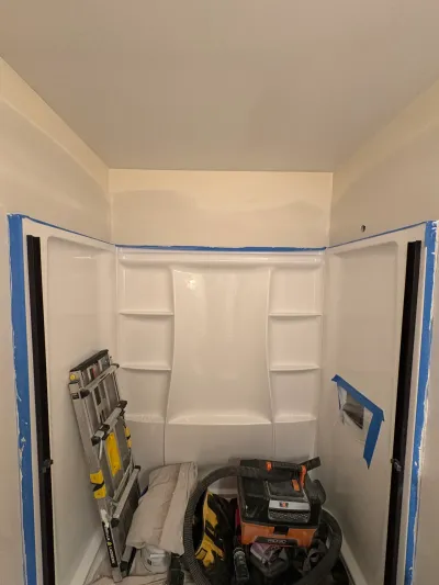 White one-piece shower surround newly installed in an alcove, taped off, with a ladder and shop vac inside.
