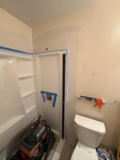 New white tub and shower surround masked with blue tape during a small bathroom renovation, toilet at right.