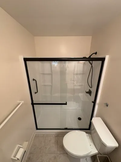 White acrylic alcove shower with matte black sliding glass doors and fixtures beside a white toilet.