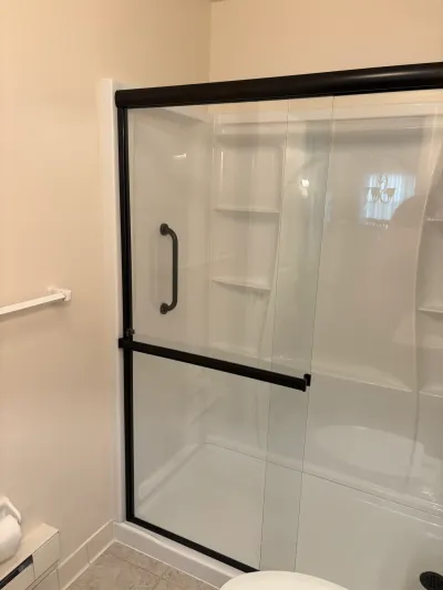 White acrylic alcove shower with matte black framed sliding glass doors and built-in corner shelves.