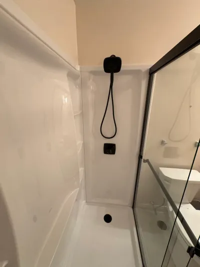 White acrylic walk-in shower with matte black handheld shower head and black-framed sliding glass door.