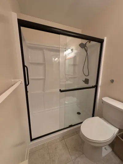 White acrylic alcove shower with bronze sliding glass doors beside a white toilet on tile flooring.