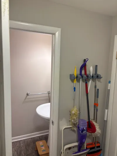 Hallway with a cleaning supply organizer beside an open bathroom door showing a pedestal sink.